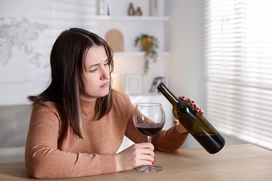 Photo of Alcohol addiction. Miserable woman pouring wine into glass at table indoors