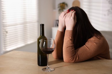 Photo of Alcohol addiction. Miserable woman with wine at table indoors