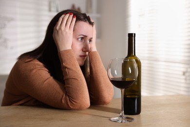 Photo of Alcohol addiction. Miserable woman with wine at table indoors, selective focus