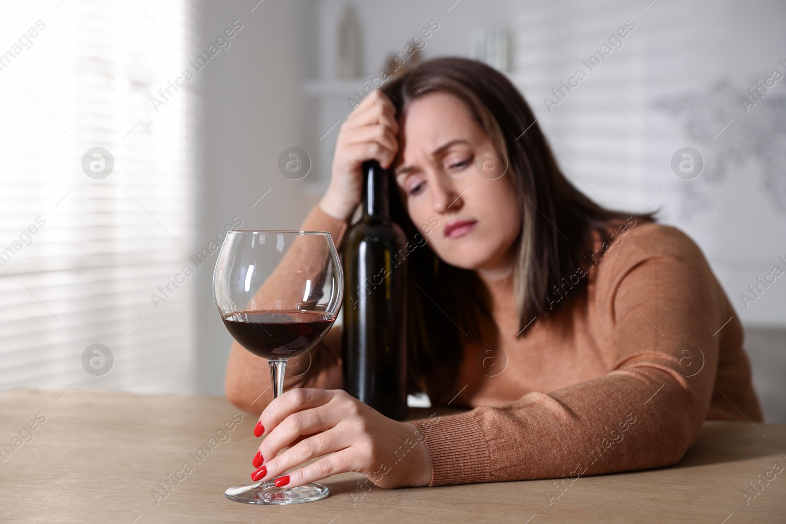 Photo of Alcohol addiction. Miserable woman with wine at table indoors, selective focus