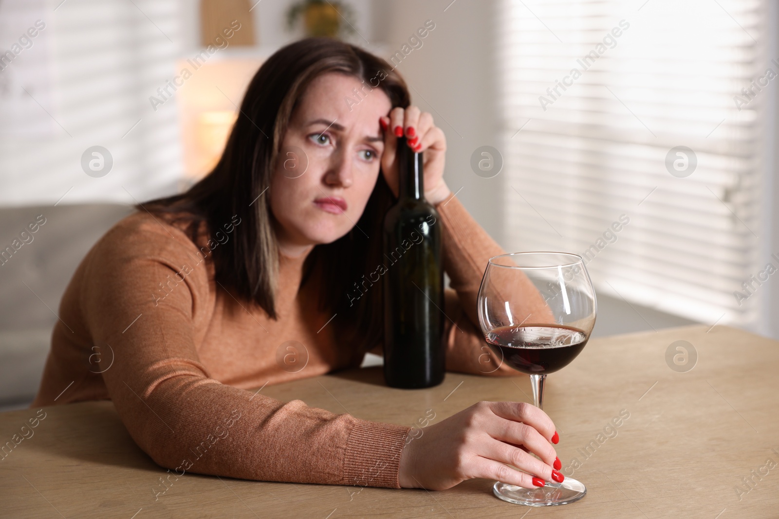 Photo of Alcohol addiction. Miserable woman with wine at table indoors, selective focus