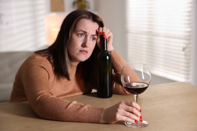 Photo of Alcohol addiction. Miserable woman with wine at table indoors, selective focus