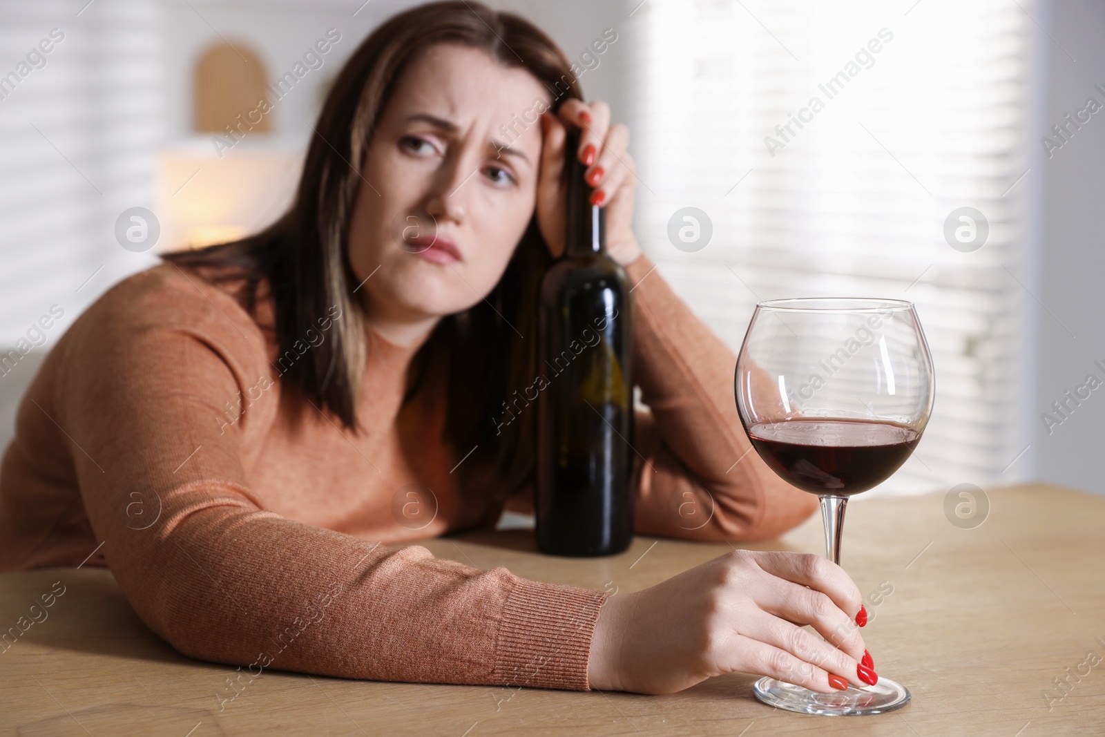 Photo of Alcohol addiction. Miserable woman with wine at table indoors, selective focus