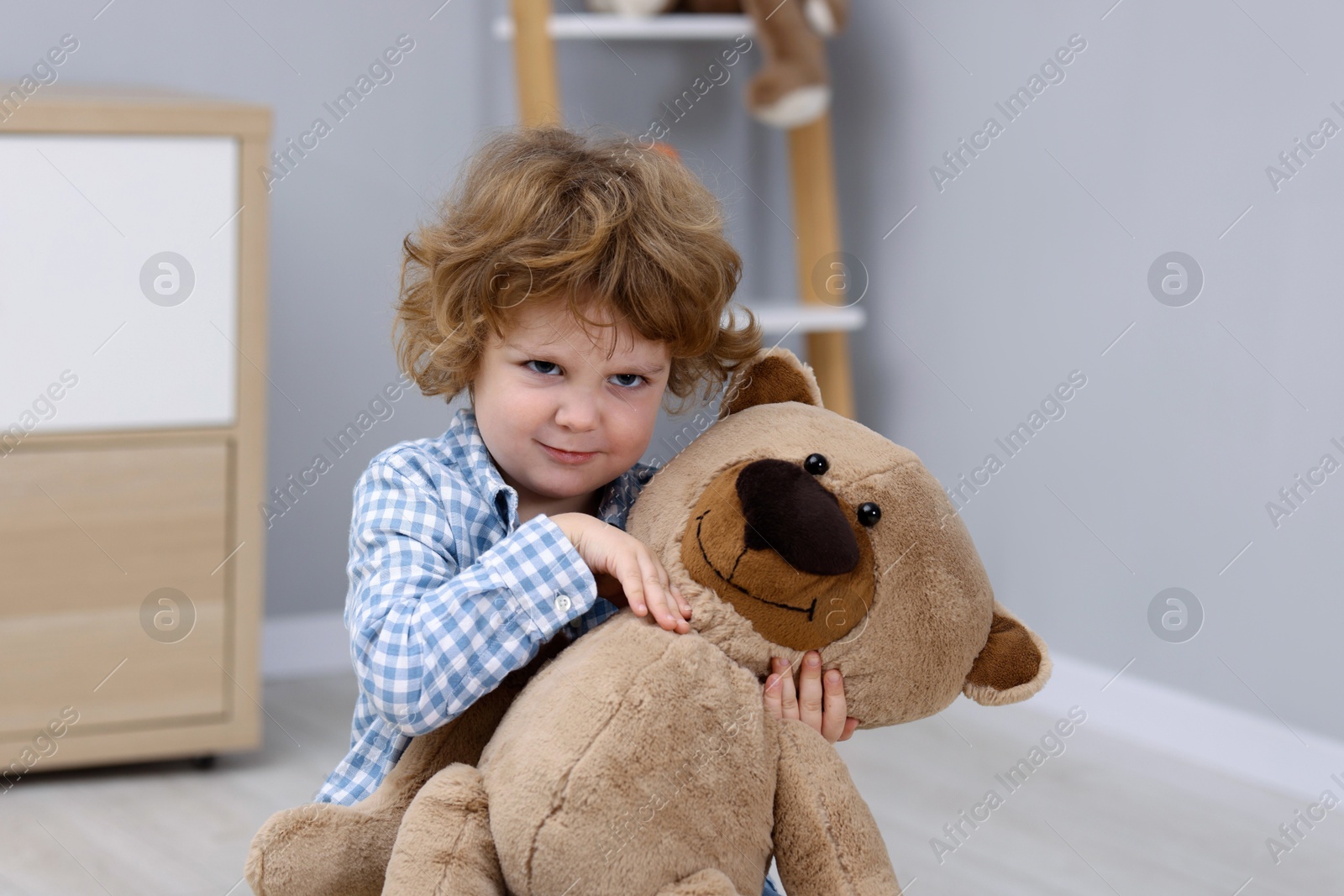 Photo of Resentful little boy with teddy bear indoors