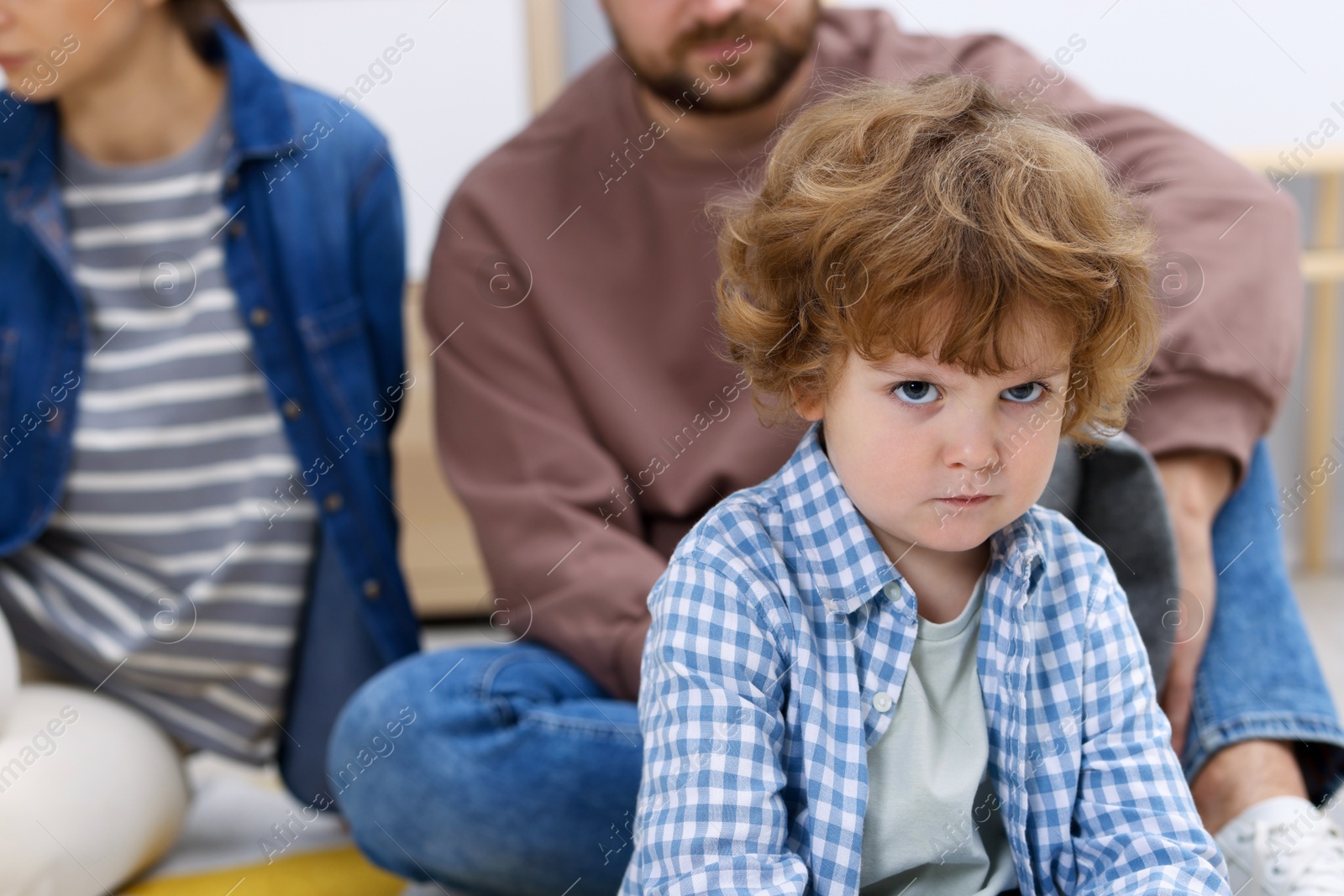 Photo of Resentful little boy and his parents arguing at home