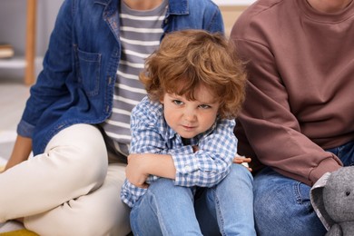 Photo of Resentful little boy and his parents arguing at home