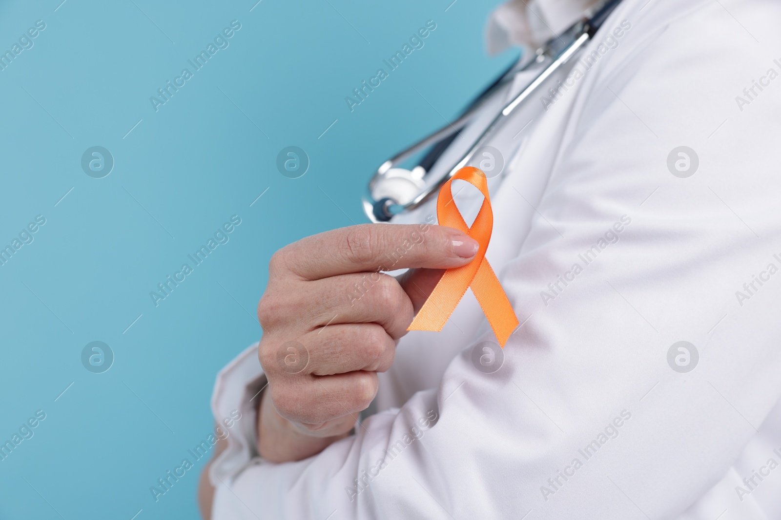 Photo of Multiple Sclerosis awareness. Doctor with orange ribbon on light blue background, closeup