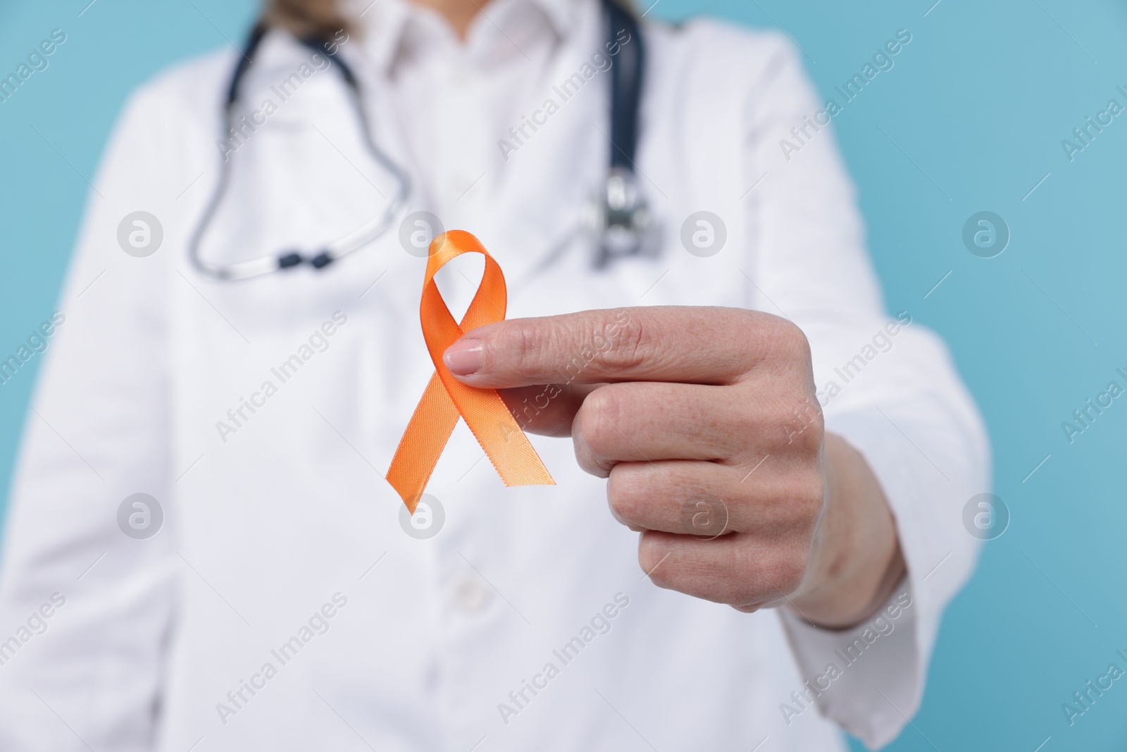 Photo of Multiple Sclerosis awareness. Doctor with orange ribbon on light blue background, closeup