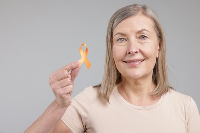 Photo of Multiple Sclerosis awareness. Woman with orange ribbon on light grey background