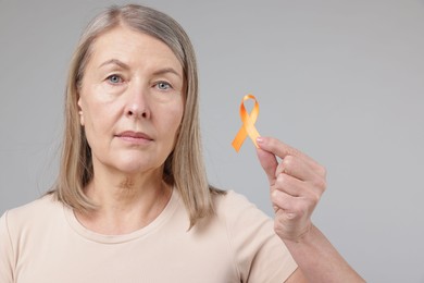 Photo of Multiple Sclerosis awareness. Woman with orange ribbon on light grey background