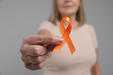 Photo of Multiple Sclerosis awareness. Woman with orange ribbon on light grey background, closeup