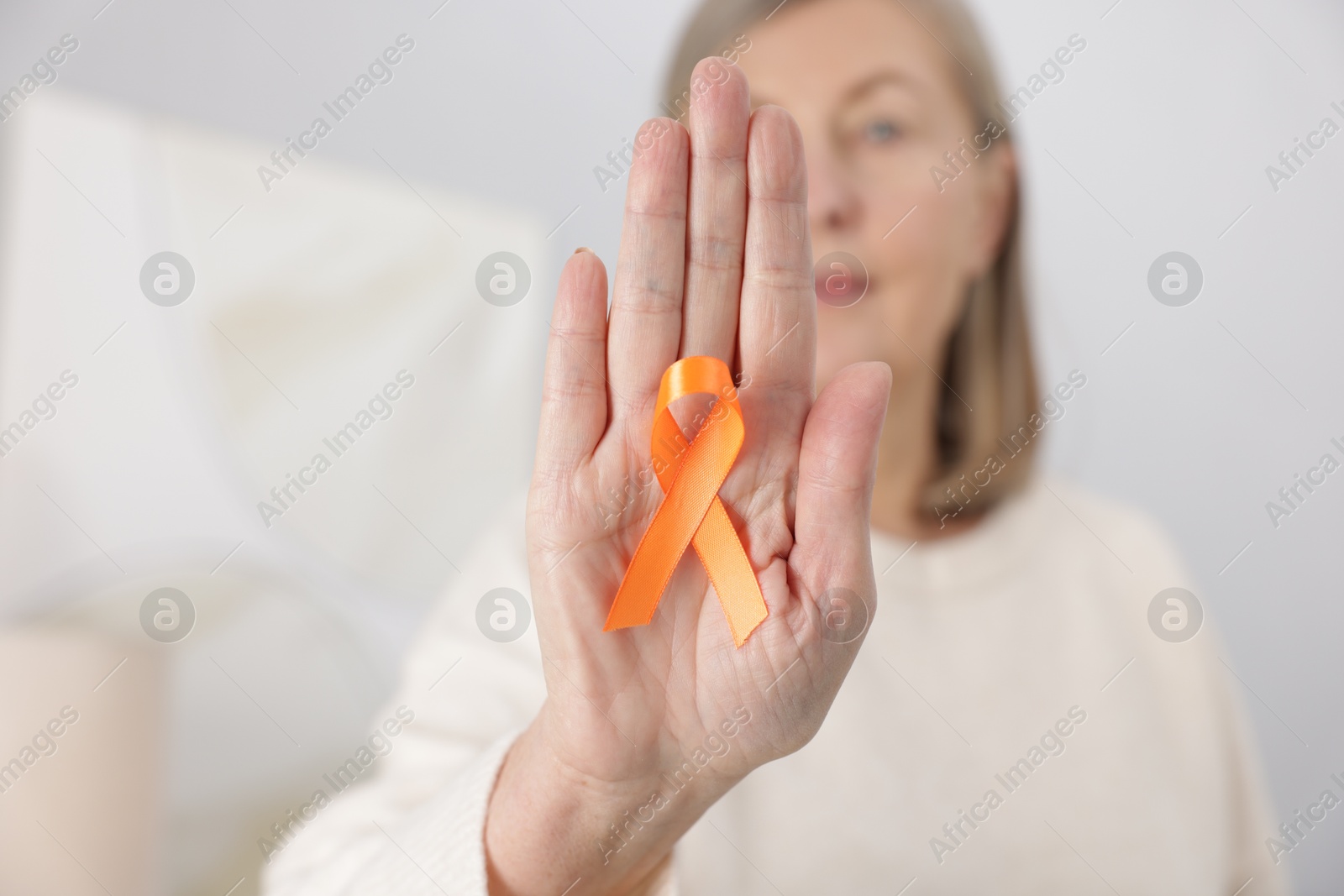 Photo of Multiple Sclerosis awareness. Woman with orange ribbon at home, selective focus