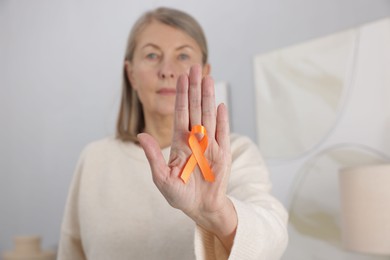 Photo of Multiple Sclerosis awareness. Woman with orange ribbon at home, selective focus