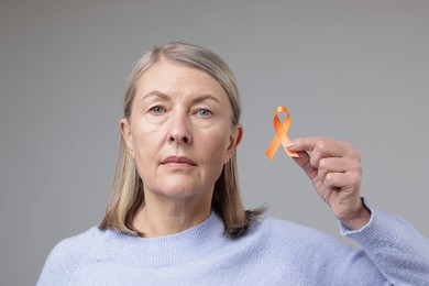 Multiple Sclerosis awareness. Woman with orange ribbon on light grey background