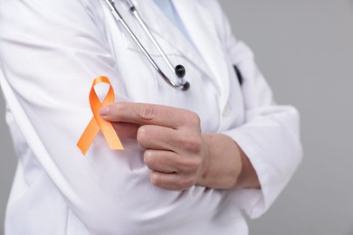 Photo of Multiple Sclerosis awareness. Doctor with orange ribbon on light grey background, closeup