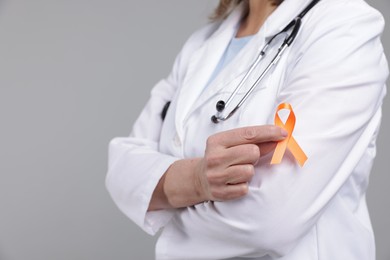 Photo of Multiple Sclerosis awareness. Doctor with orange ribbon on light grey background, closeup