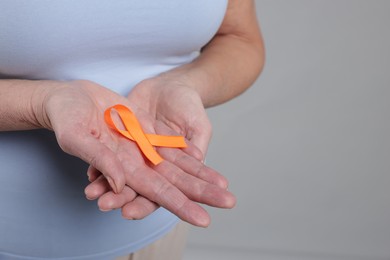 Photo of Multiple Sclerosis awareness. Woman with orange ribbon on light grey background, closeup