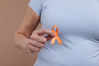 Photo of Multiple Sclerosis awareness. Woman with orange ribbon on brown background, closeup