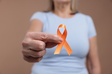 Photo of Multiple Sclerosis awareness. Woman with orange ribbon on brown background, closeup