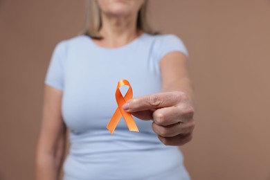 Photo of Multiple Sclerosis awareness. Woman with orange ribbon on brown background, closeup