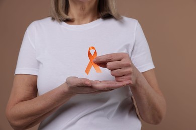 Multiple Sclerosis awareness. Woman with orange ribbon on brown background, closeup