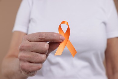 Photo of Multiple Sclerosis awareness. Woman with orange ribbon on brown background, closeup