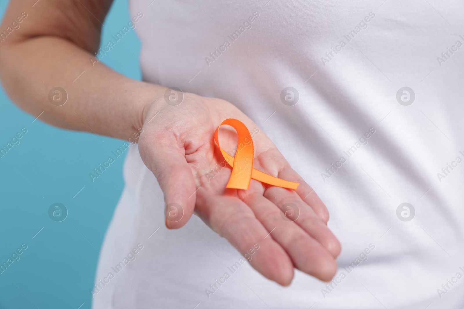 Photo of Multiple Sclerosis awareness. Woman with orange ribbon on light blue background, closeup