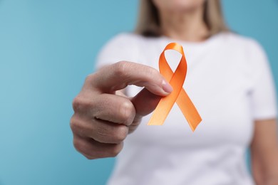 Photo of Multiple Sclerosis awareness. Woman with orange ribbon on light blue background, closeup