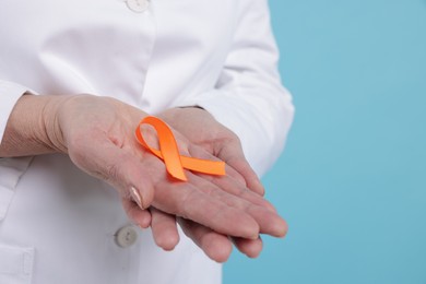 Photo of Multiple Sclerosis awareness. Doctor with orange ribbon on light blue background, closeup