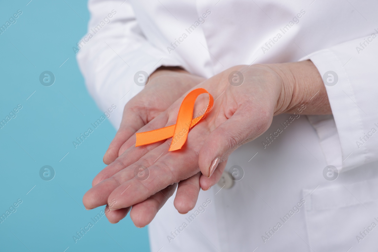 Photo of Multiple Sclerosis awareness. Doctor with orange ribbon on light blue background, closeup