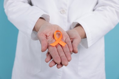 Photo of Multiple Sclerosis awareness. Doctor with orange ribbon on light blue background, closeup