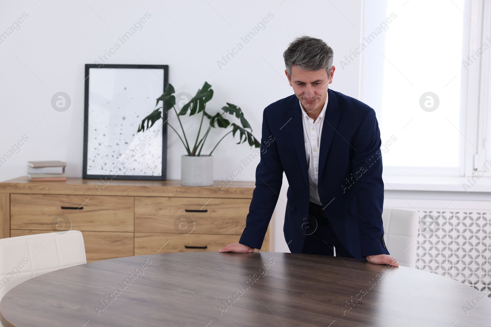 Photo of Man looking at something on desk in office. Space for text