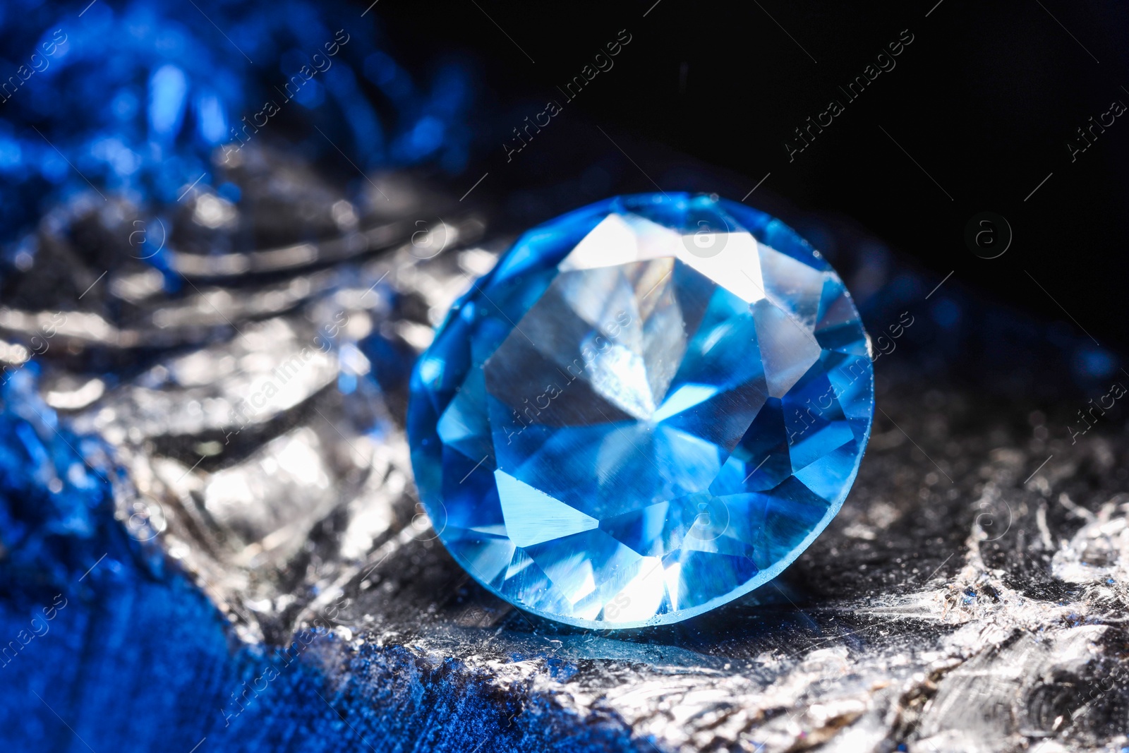 Photo of Beautiful shiny light blue gemstone on stone against black background, closeup