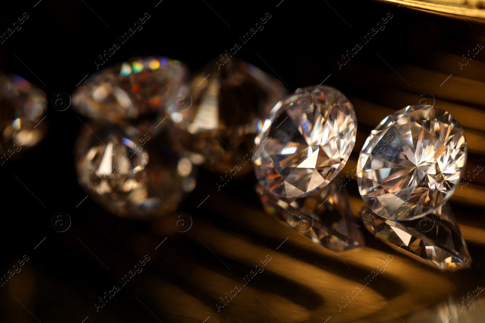 Photo of Beautiful shiny gemstones on golden tray in dark, closeup