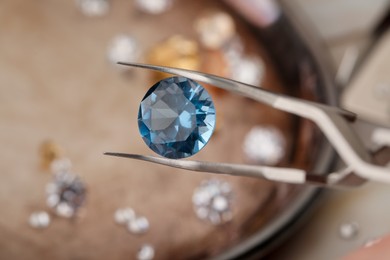 Photo of Tweezers with beautiful gemstone on blurred background, closeup