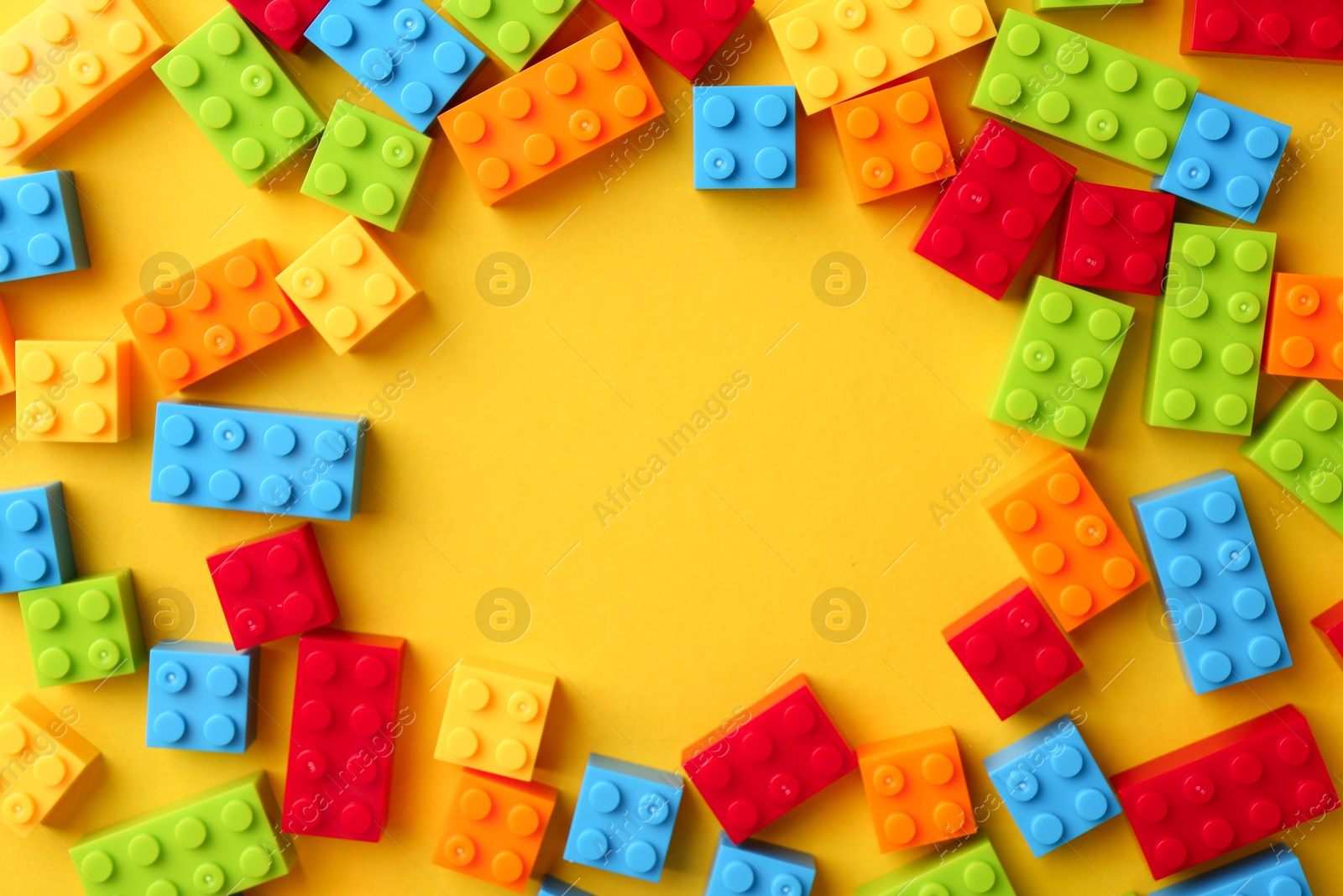 Photo of Constructor toy. Frame made of many colorful building blocks on yellow background, flat lay. Space for text