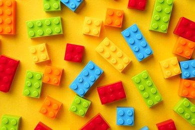 Photo of Constructor toy. Many colorful building blocks on yellow background, flat lay