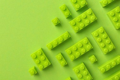 Photo of Constructor toy. Many building blocks on light green background, flat lay. Space for text