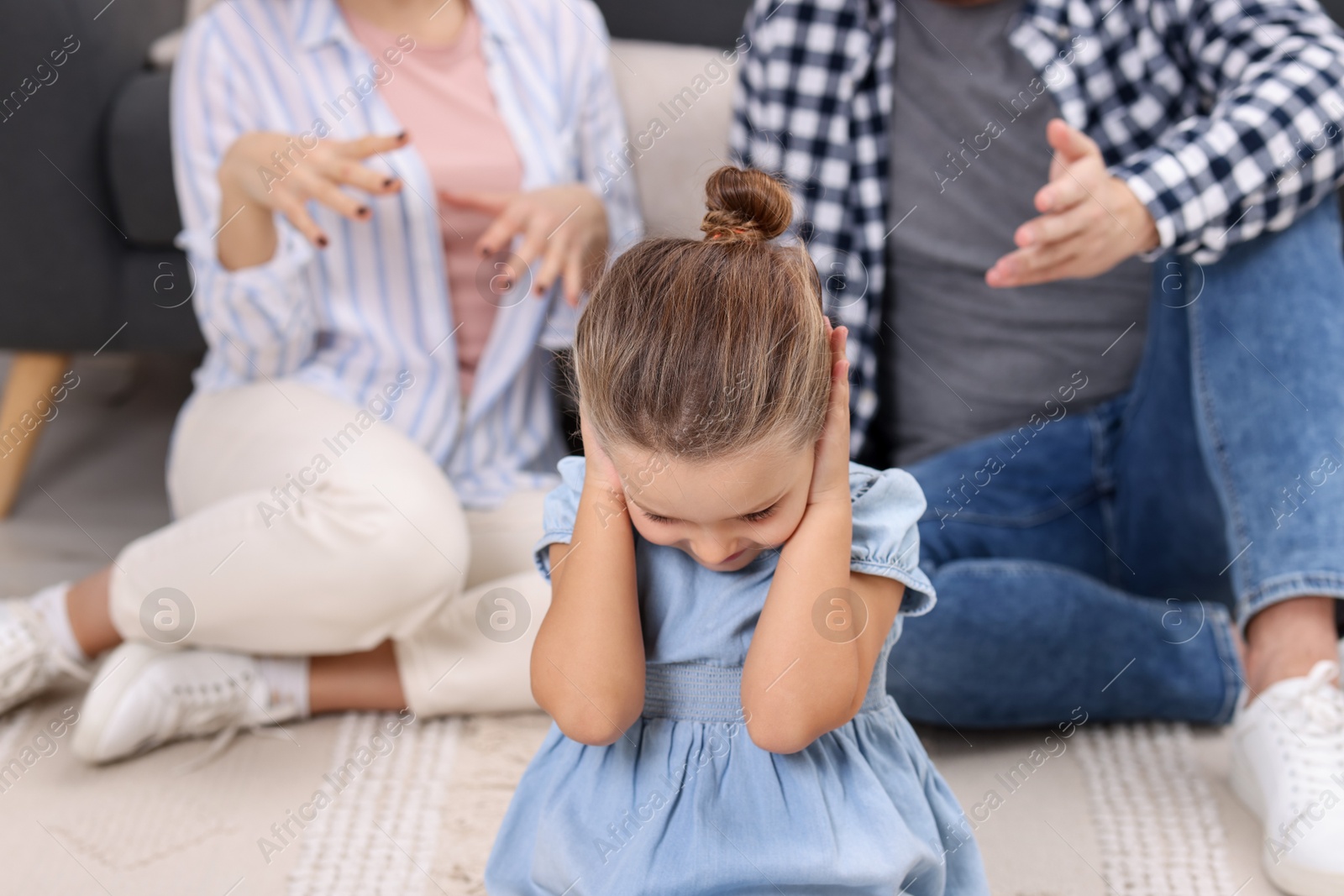 Photo of Resentful little girl covering ears near her parents at home. Family dispute