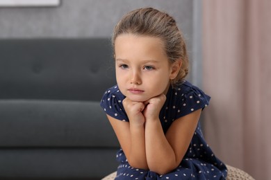 Photo of Resentful little girl sitting on pouf at home