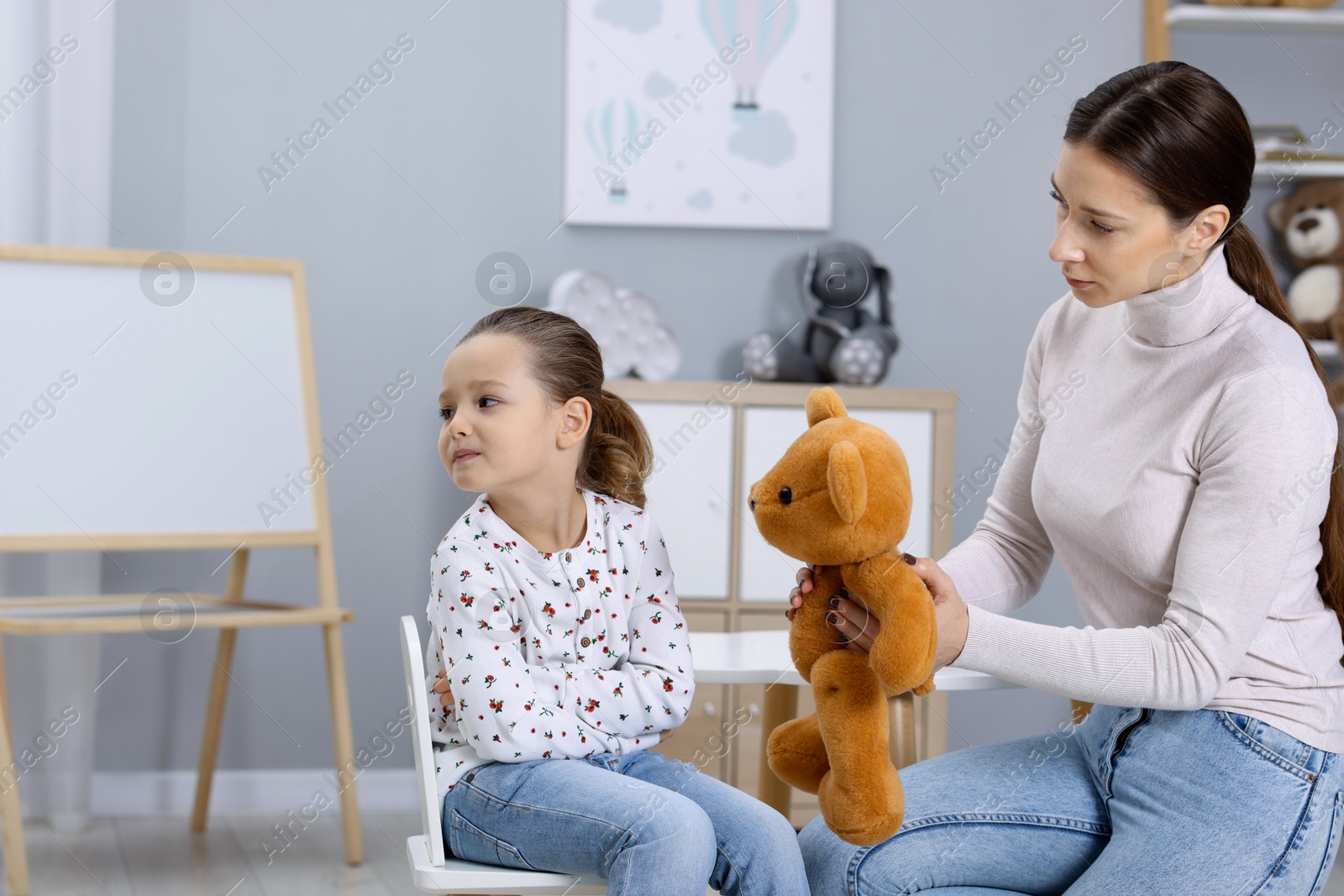 Photo of Resentful little girl and her mother with teddy bear at home. Family dispute