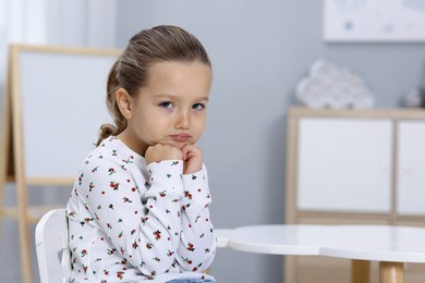 Photo of Resentful little girl at white table indoors, space for text