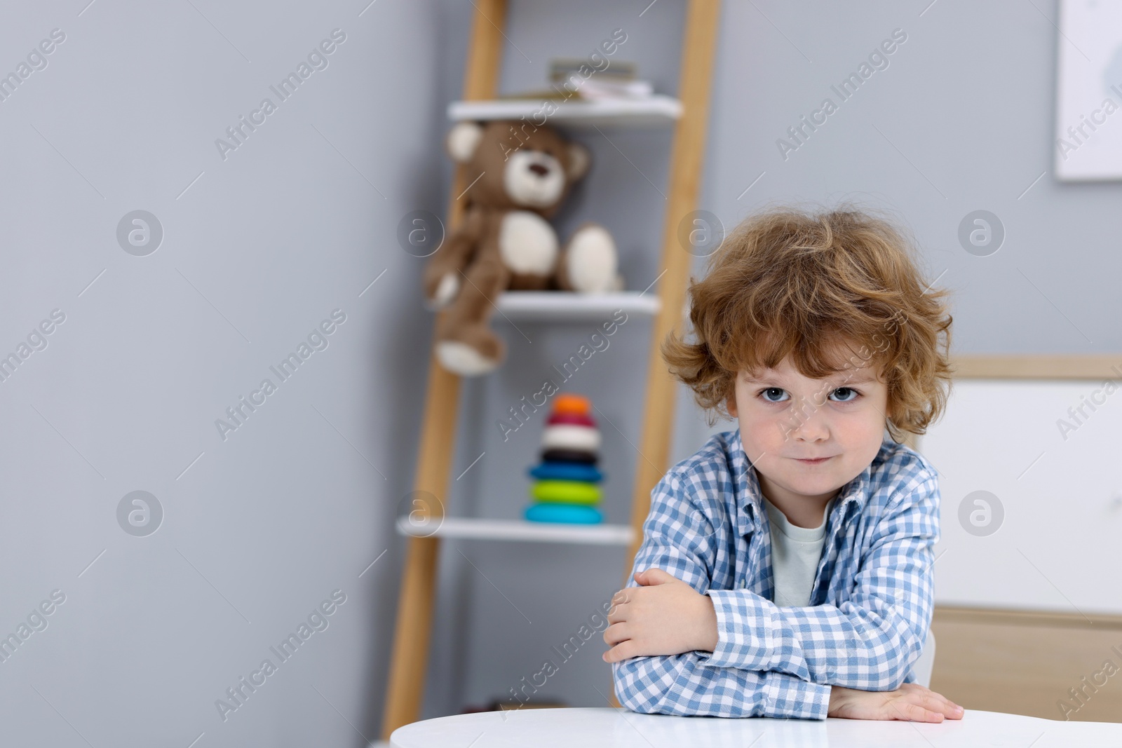 Photo of Resentful little boy at white table indoors, space for text