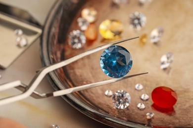 Photo of Tweezers with beautiful gemstones on light table, selective focus