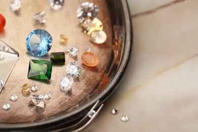 Photo of Tray with beautiful gemstones and tweezers on light table, closeup