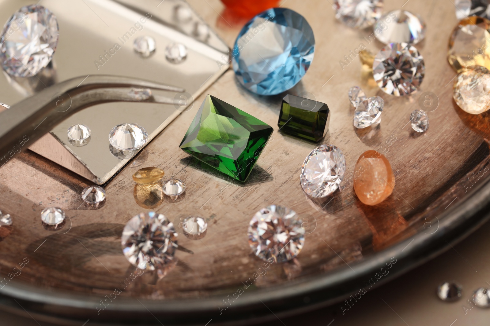 Photo of Tray with beautiful gemstones and tweezers on light table, closeup