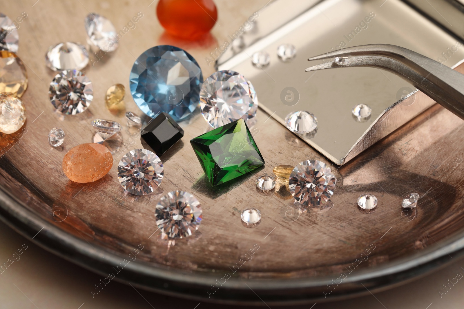 Photo of Tray with beautiful gemstones and tweezers on light table, closeup