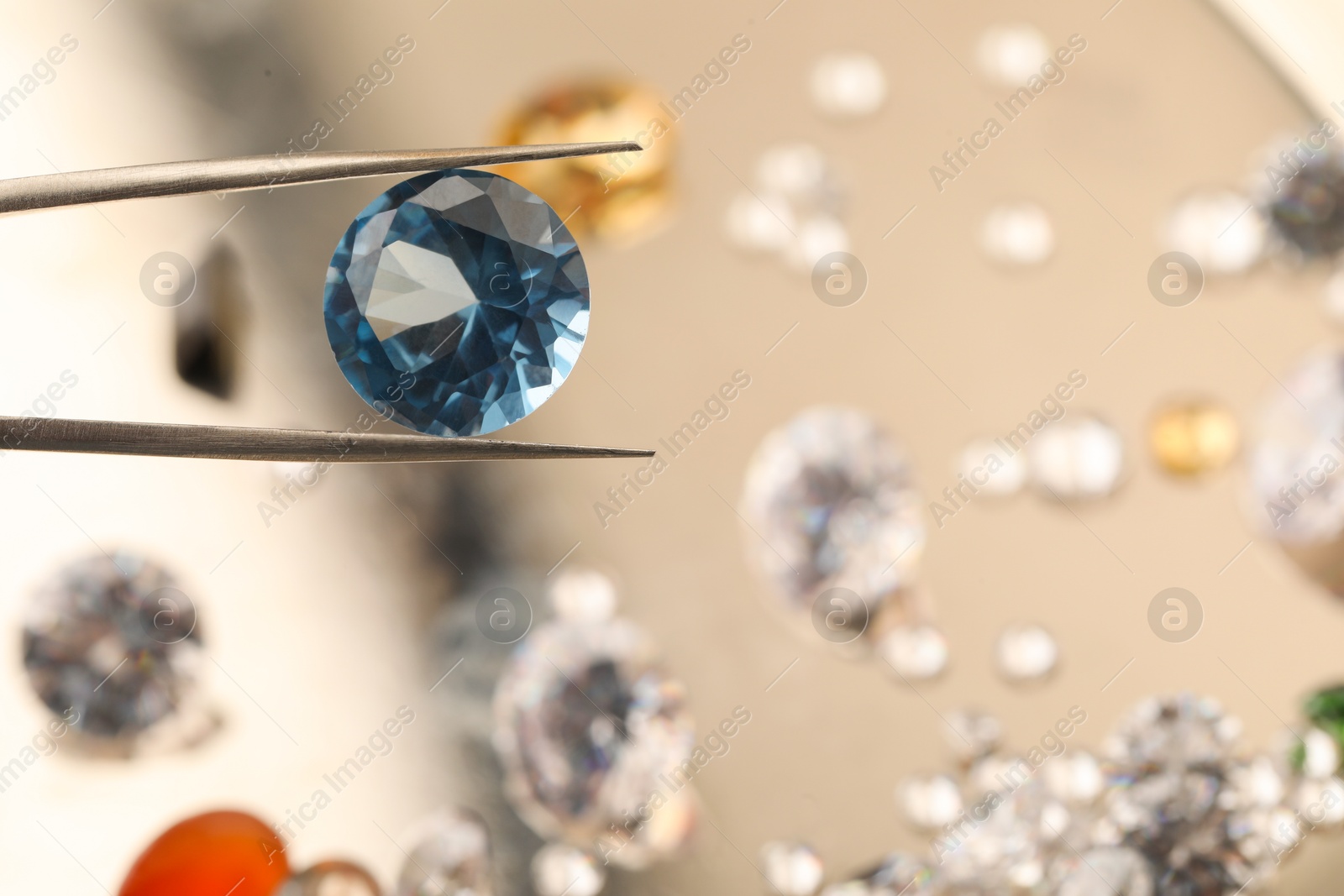 Photo of Tweezers with beautiful gemstone on blurred background, closeup