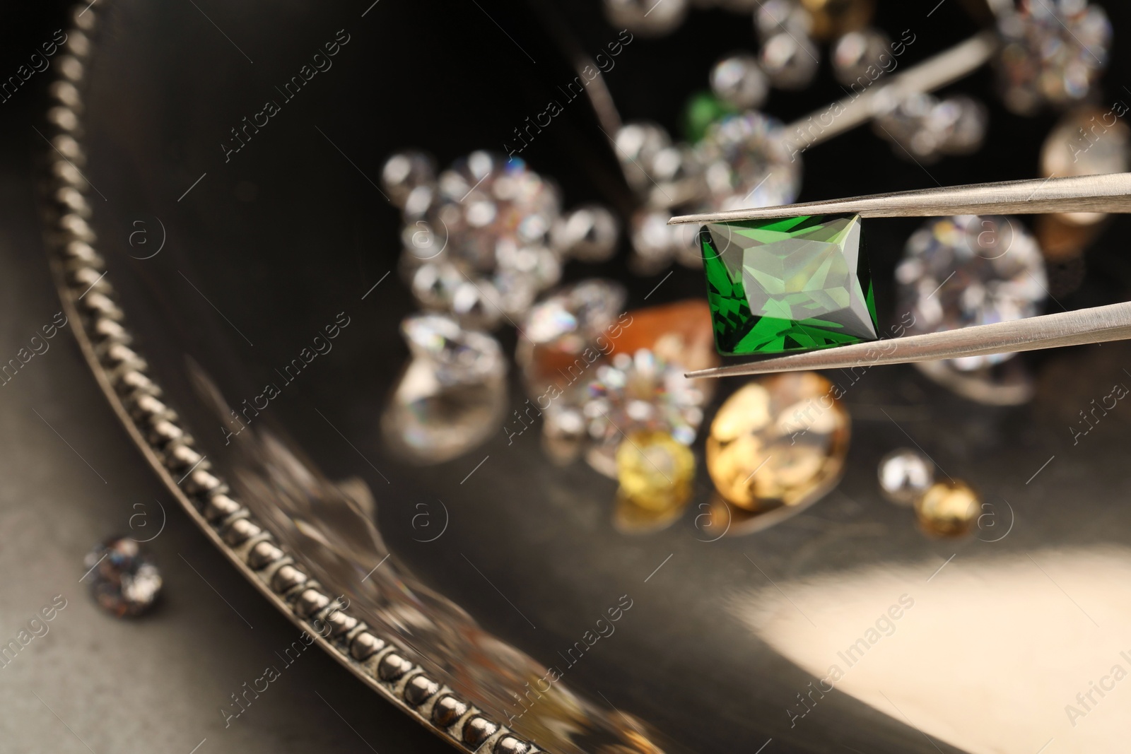 Photo of Tweezers with beautiful gemstone on blurred background, closeup