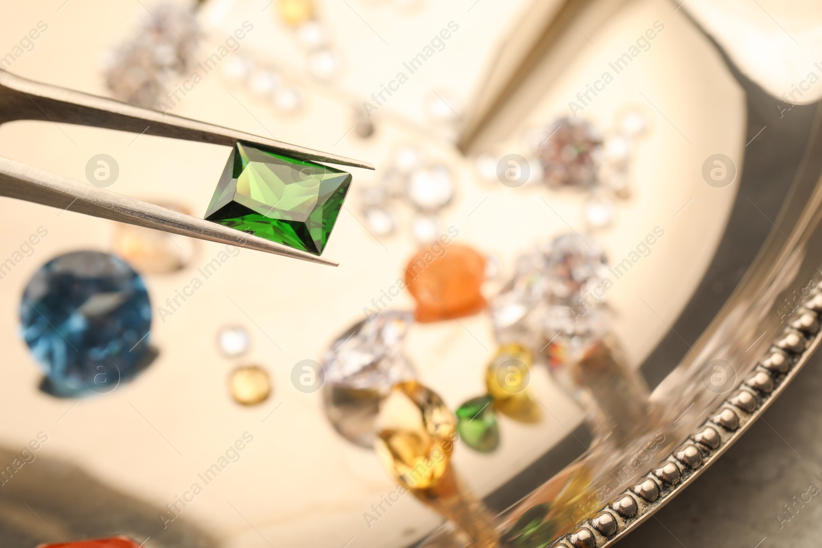 Photo of Tweezers with beautiful gemstones on light table, selective focus